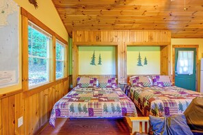 Ein Blockhauszimmer mit zwei Betten, Holzwänden und großen Fenstern.