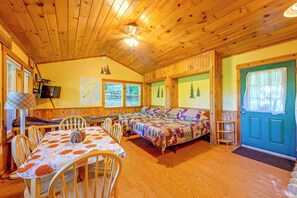 Ein gemütliches Blockhaus-Interieur mit Essbereich, einem Bett mit Patchwork-Quilt und einem Fernseher.