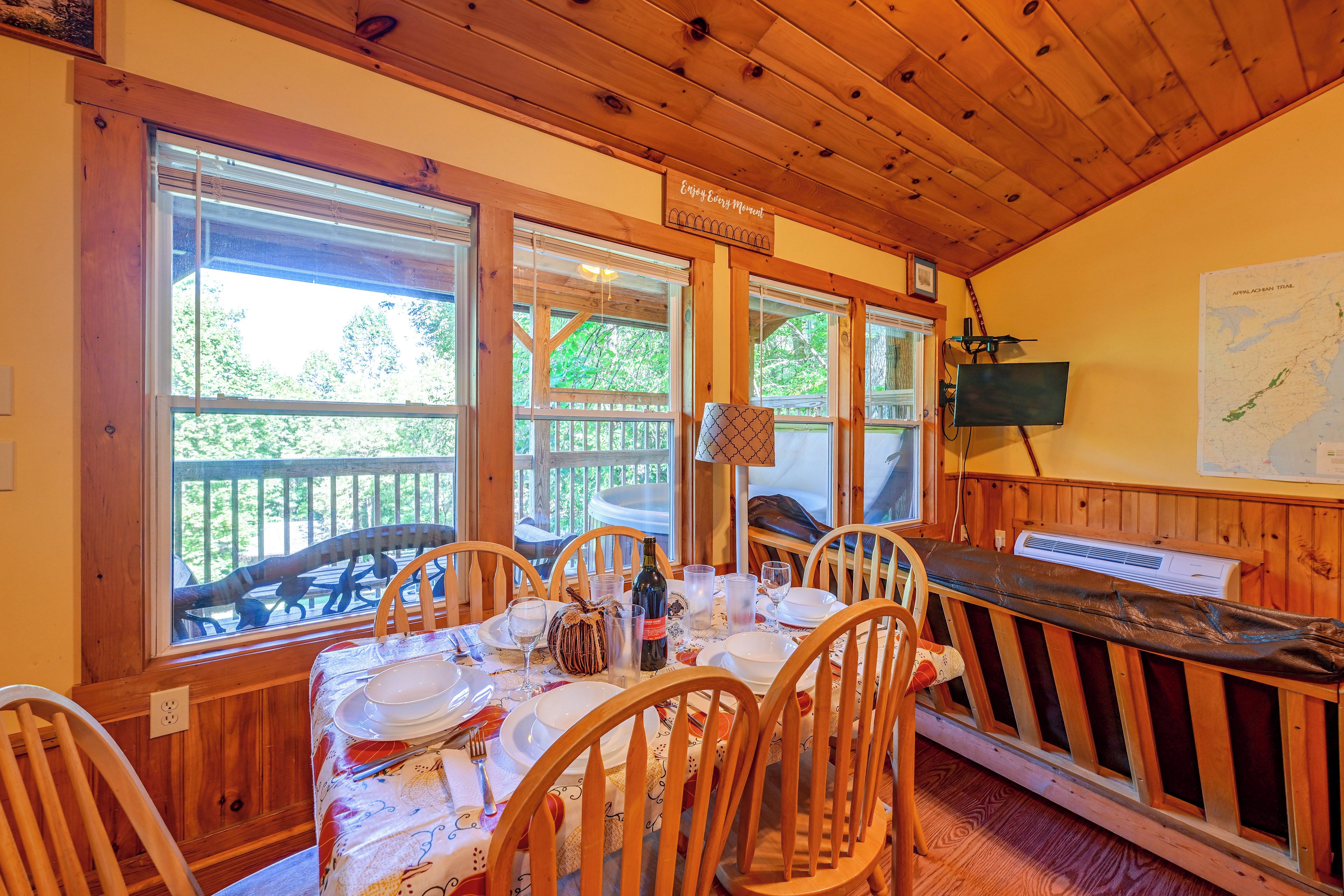 Un coin repas avec une table dressée pour quatre personnes, des chaises en bois, un banc et une carte accrochée au mur.