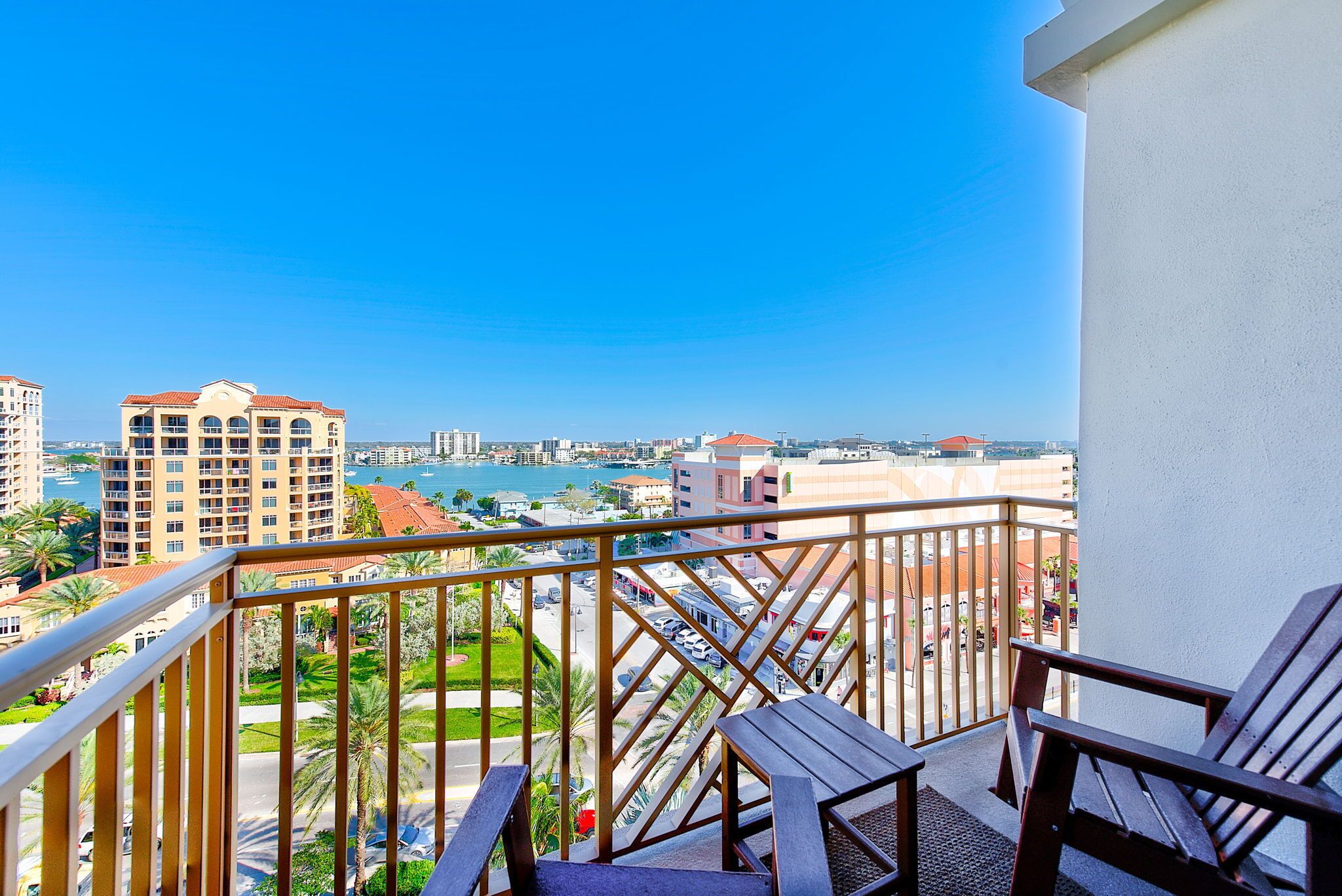 A balcony with wooden chairs, a view of a cityscape, and a clear blue sky.