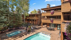 A pool area with two pools, outdoor seating, and a wooden building with balconies. - Modern Ski-in/Ski-out Condo with Pool and Hot Tub Access (Aspen)