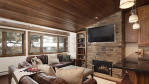 A cozy living room with a stone fireplace, leather sofas, and a flat-screen TV mounted on the wall. - Modern Ski-in/Ski-out Condo with Pool and Hot Tub Access (Aspen)