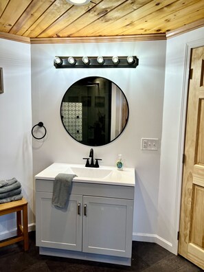 A bathroom with a white vanity, a round mirror, and a lighted vanity mirror.