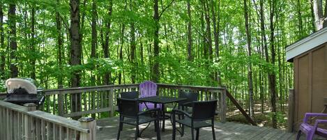 A wooden deck with a table and chairs, surrounded by a forest.