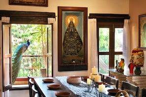 A dining area with a peacock outside, a religious painting, and a table set for dining.