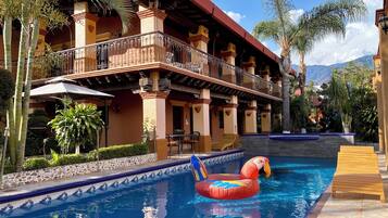 A pool with a floating flamingo decoration, surrounded by a building with balconies and palm trees.