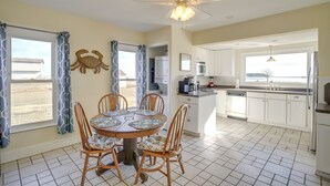 A kitchen with a dining area, white cabinets, a ceiling fan, and a view of the beach.