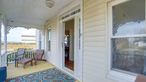A covered porch with a wooden floor, a colorful mat, and two chairs.