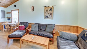 Un salon chaleureux avec un plafond en bois, un canapé, une table basse et un coin repas comprenant des chaises et une table.