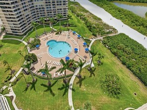 An aerial view of a hotel with a central swimming pool surrounded by lounge chairs and palm trees. - Beachfront 2BR/2BA condo with pool, WiFi, and heated pool (Marco Island)