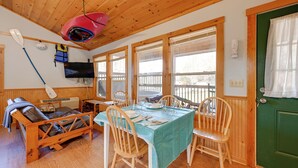 Interior acogedor de una cabaña con una mesa de comedor para cuatro, paredes de madera, una puerta verde y un televisor montado.