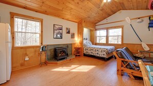 Interior acogedor de una cabaña con piso de madera, chimenea, cama y un kayak.