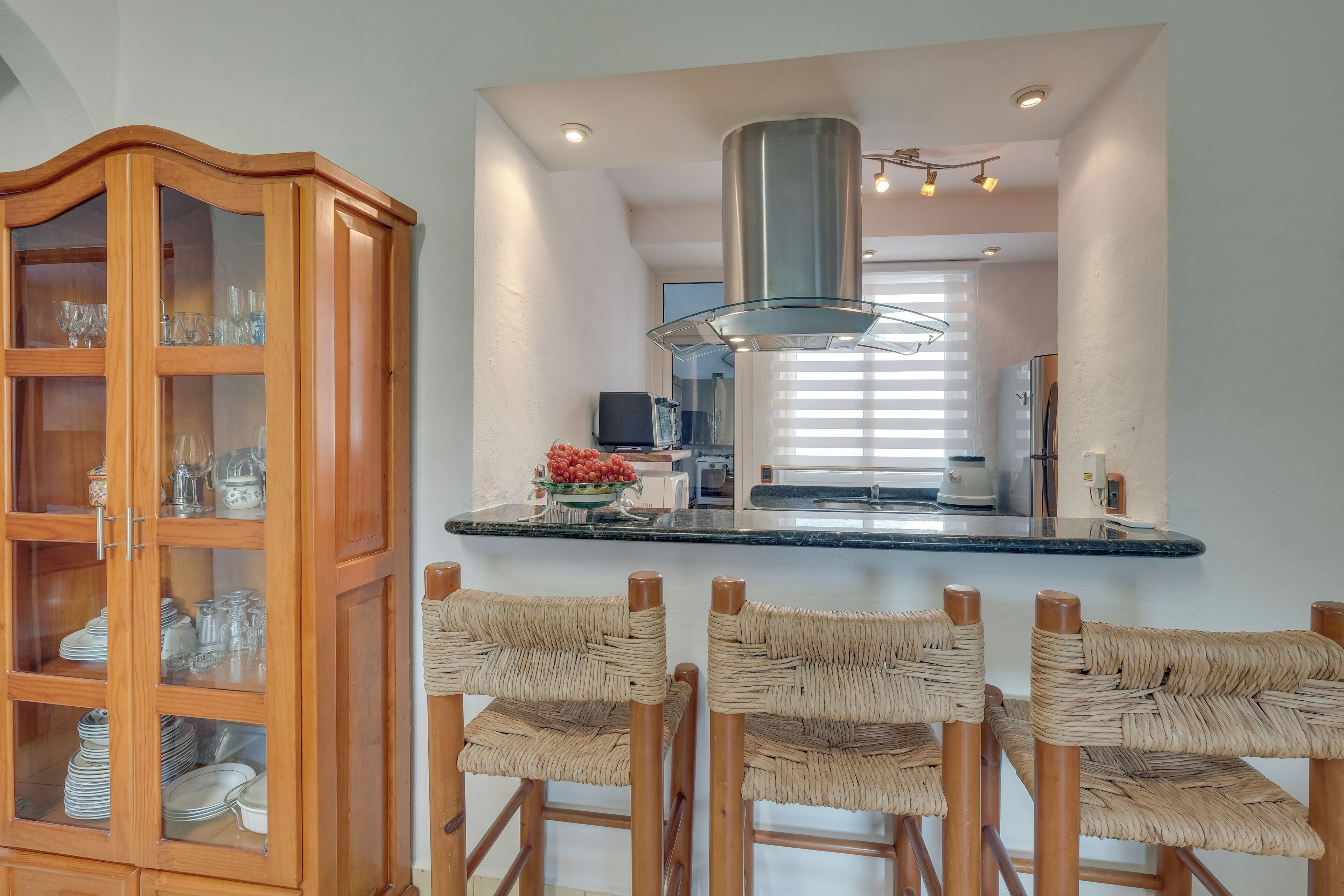Una cucina con un armadietto in legno, una cappa aspirante in acciaio inossidabile e un'area bar con sedie in vimini.