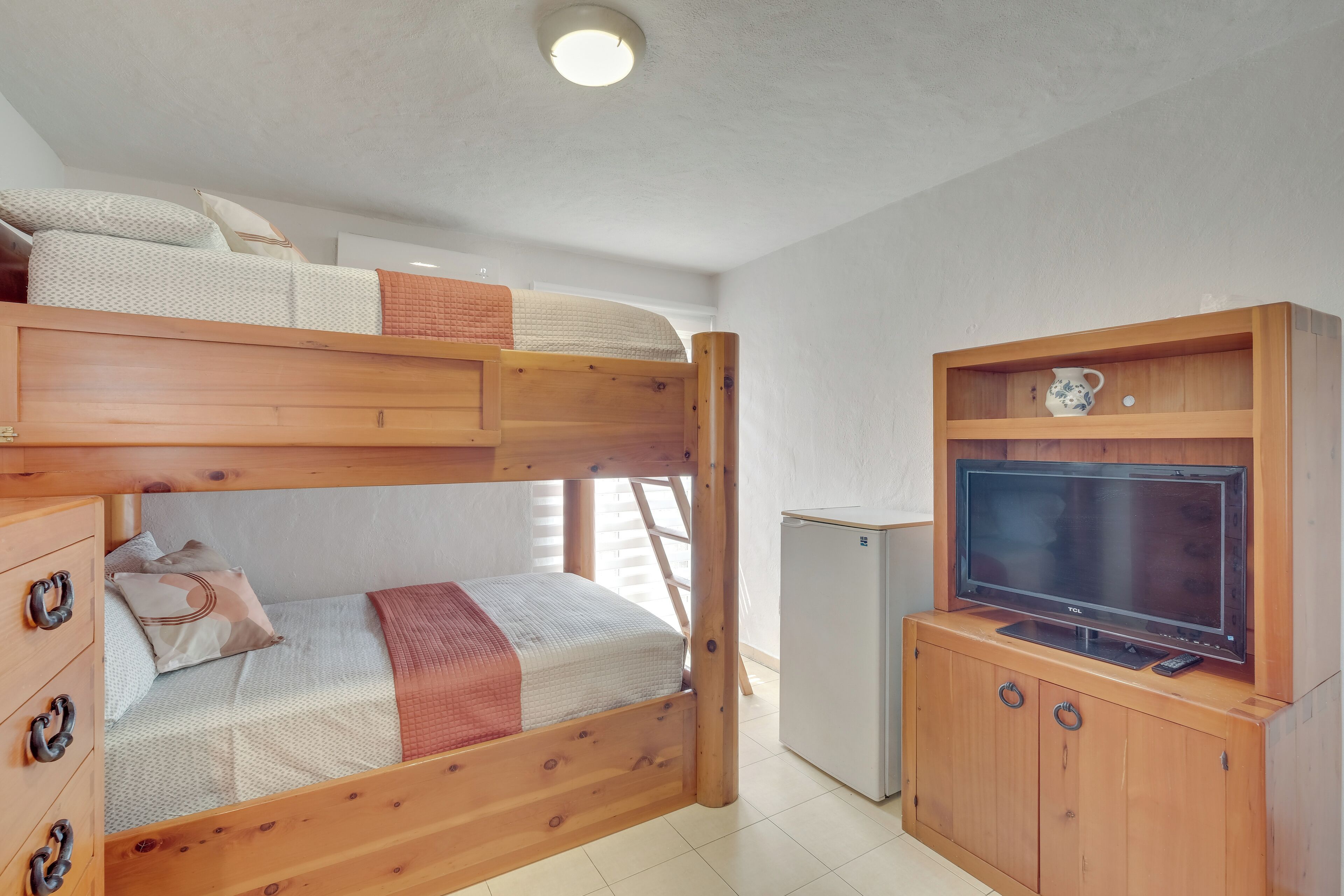 A bunk bed with a TV and storage unit in a room with white walls and a ceiling light.