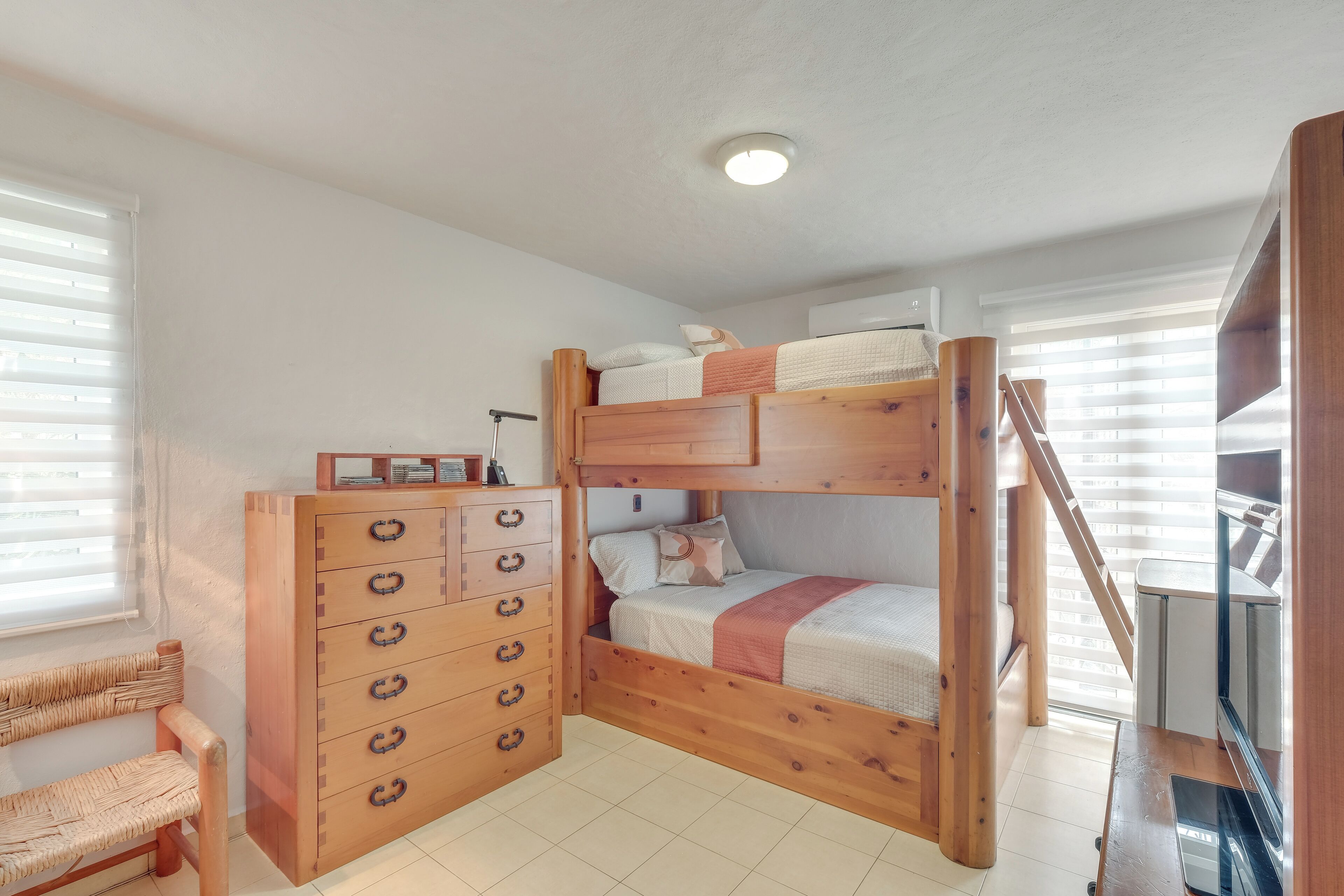 A bunk bed with a wooden dresser, a chair, and a staircase leading to an upper level.