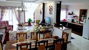 A dining area with a wooden table and chairs, a chandelier, and a television. - Chalé Stillo (Gramado)