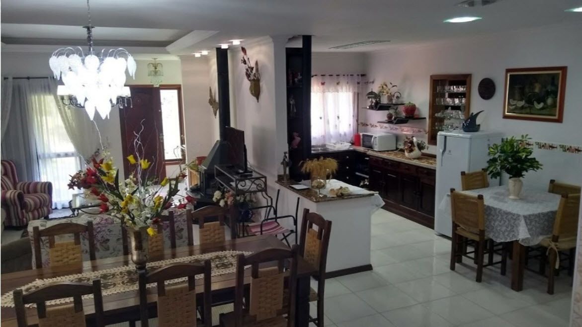 A dining area with a chandelier, a piano, and a kitchen in the background.