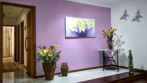 A hallway with a purple wall, a painting of flowers, a vase with flowers, a small table with a vase, and butterfly wall art. - Chalé Stillo (Gramado)