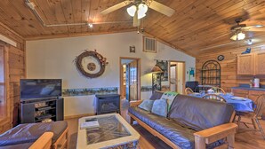 Interior acogedor de una cabaña con techo de madera, chimenea, televisor, sofá y comedor.