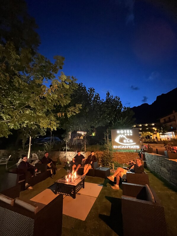 An outdoor seating area with a fire pit, surrounded by stone walls and trees.