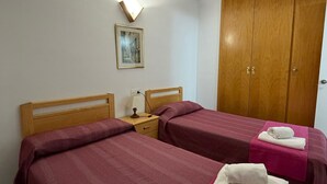 Ein Hotelzimmer mit zwei Betten, einem Holzschrank, einem Nachttisch mit Lampe und einem gerahmten Bild an der Wand.