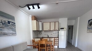 Ein kompakter Wohnbereich mit Sofa, Esstisch, Küchenzeile und kleinem Kühlschrank.