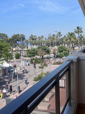 A balcony with a view of a busy street, palm trees, and a distant beach. - Sant Jordi Zeus Salou 33202 (Salou)