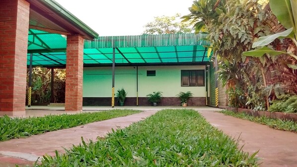 Um pátio com um edifício de telhado verde, plantas em vasos e um caminho de tijolos.