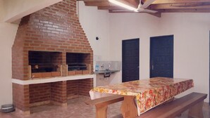 A room with a brick fireplace, a wooden table with a floral tablecloth, and two dark doors. - Apart hotel Las Guayabas (Puerto Iguazú)