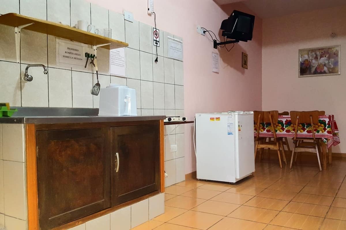 A kitchen with a wooden cabinet, a white refrigerator, a microwave, and a small sink. There is a table with a checkered tablecloth and chairs.