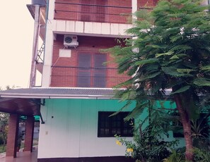 Um edifício de vários andares com fachada verde e branca, aparelhos de ar condicionado na parte externa e uma varanda com corrimão de metal.