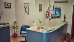 A reception area with a blue desk, a chair, potted plants, and various framed pictures on the walls. - Apart hotel Las Guayabas (Puerto Iguazú)