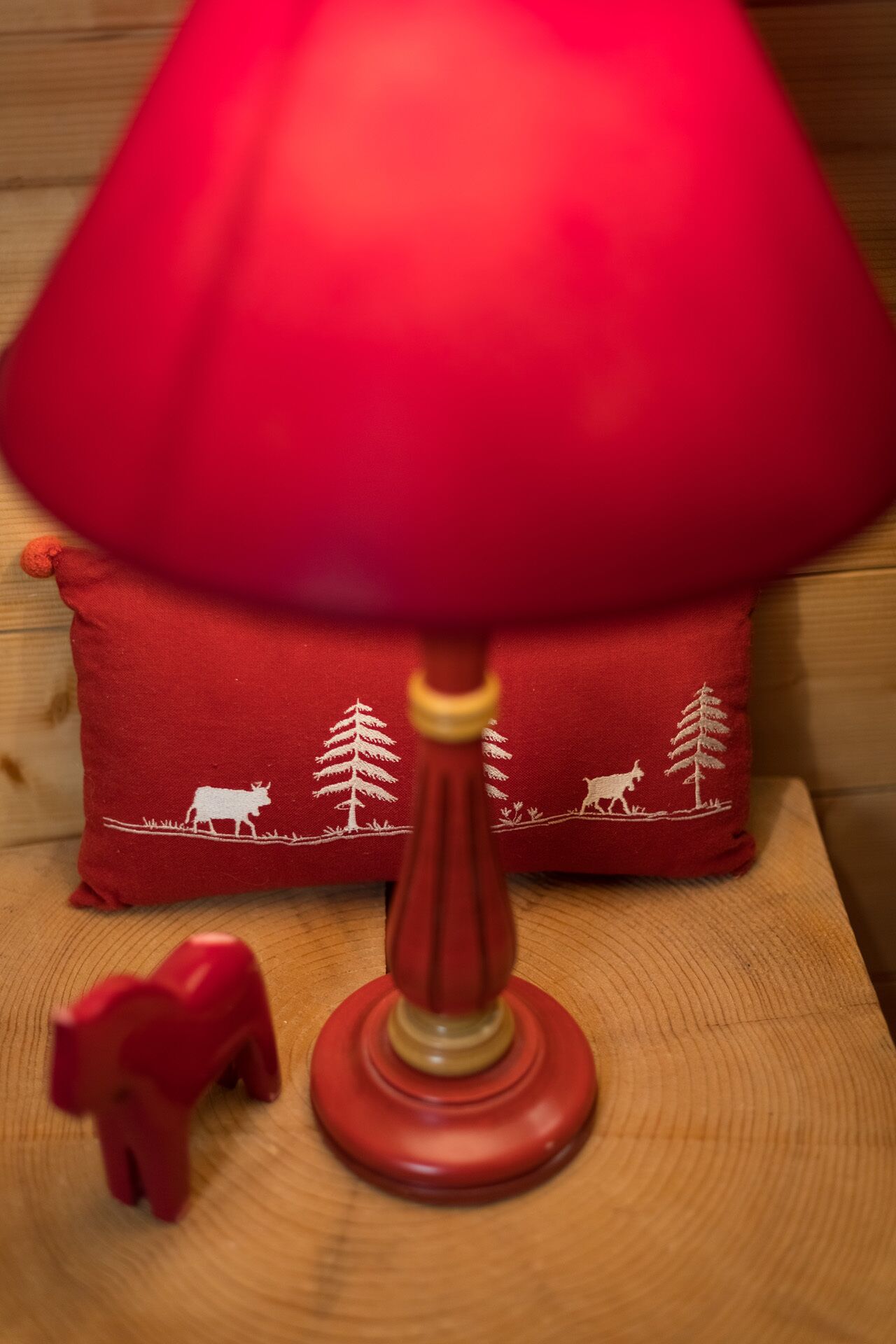 Une lampe rouge avec un pied en bois et un coussin rouge orné de broderies blanches.
