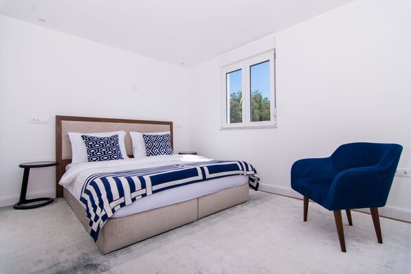 A bedroom with a bed, a blue chair, a window, and a nightstand. - Penthouse Deep Blue near Trogir (Trogir)