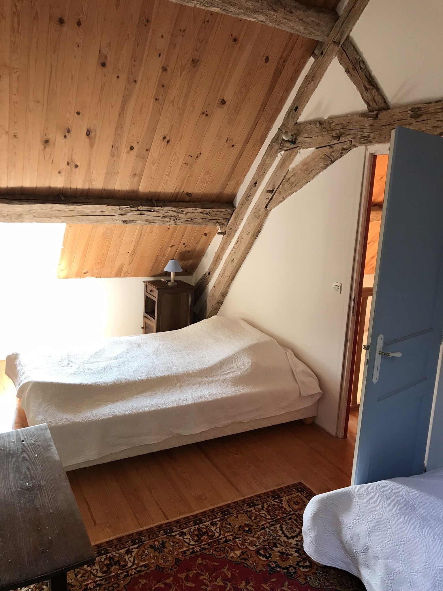 A small, cozy bedroom with a sloped ceiling, a single bed, a nightstand, a lamp, and a door.