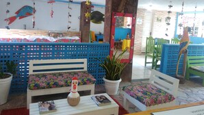 A room with a bed, a table with a magazine, a decorative rooster, and a mirror with a colorful frame. - Pousada Aquários do Porto (Ipojuca)