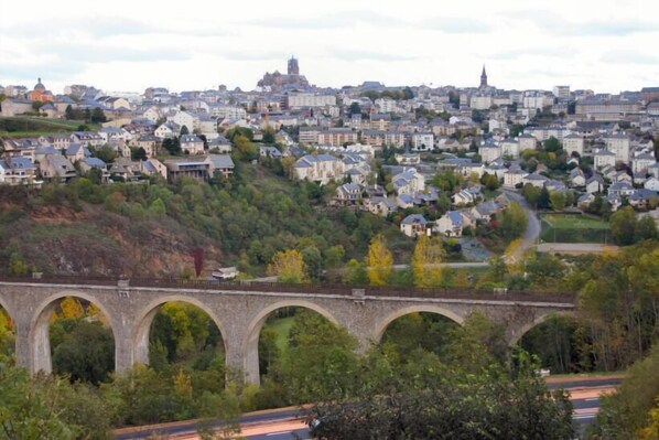 A stone bridge with multiple arches over a road, with a cityscape in the background.