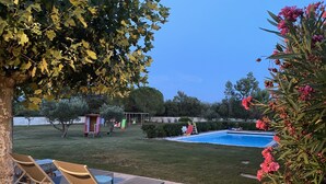 Ein Garten mit Swimmingpool, einer kleinen Spielgegend und einem Baum, der Schatten spendet.