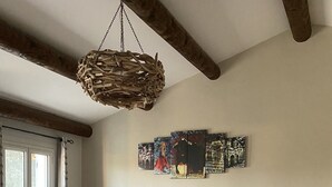 Ein Schlafzimmer mit Bett, Holz-Kopfteil, Pendelleuchte, Heizkörper, Fenster und Wand mit Kunstwerken.