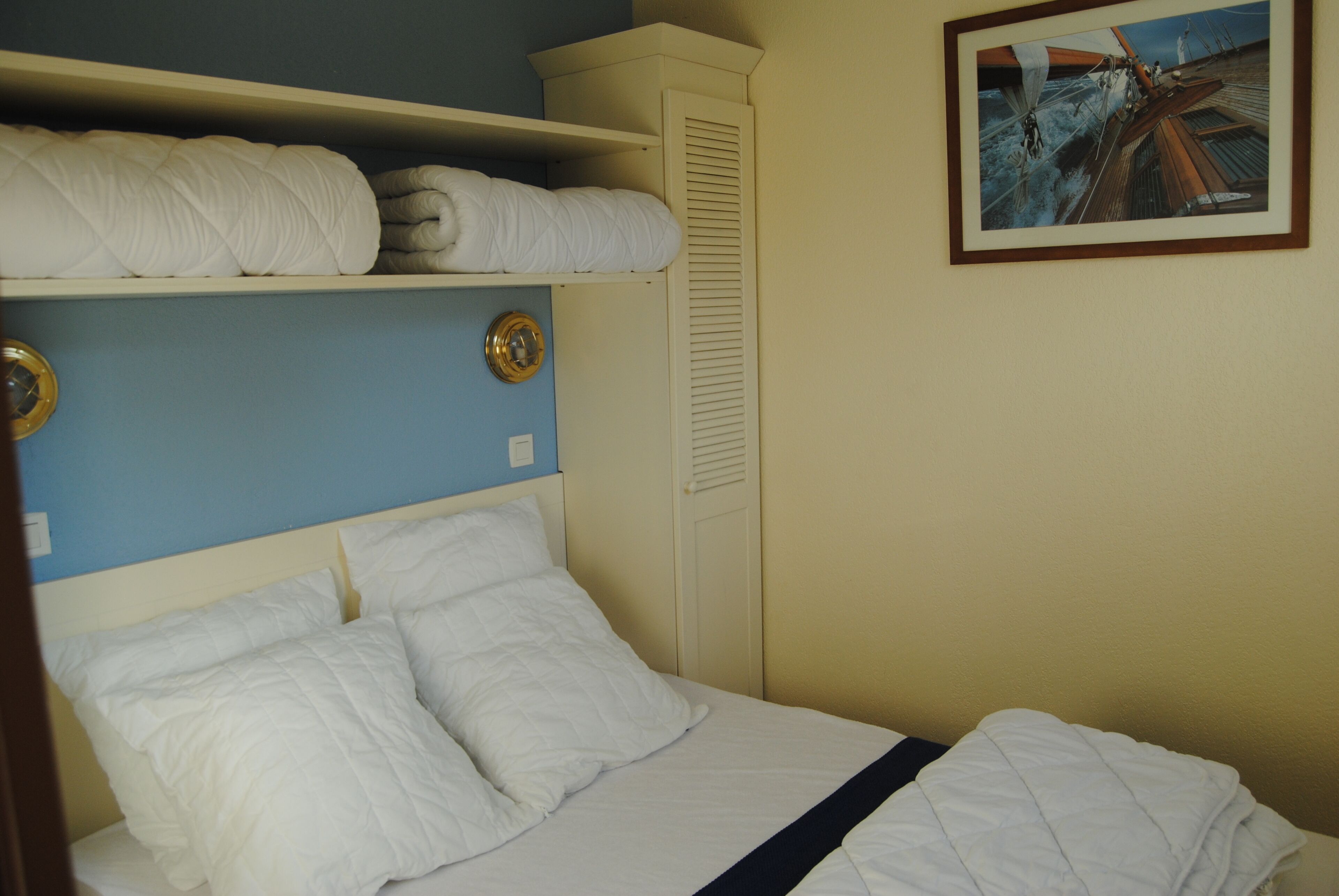 A neatly made bed with white bedding, a blue wall, and a framed picture on the wall.
