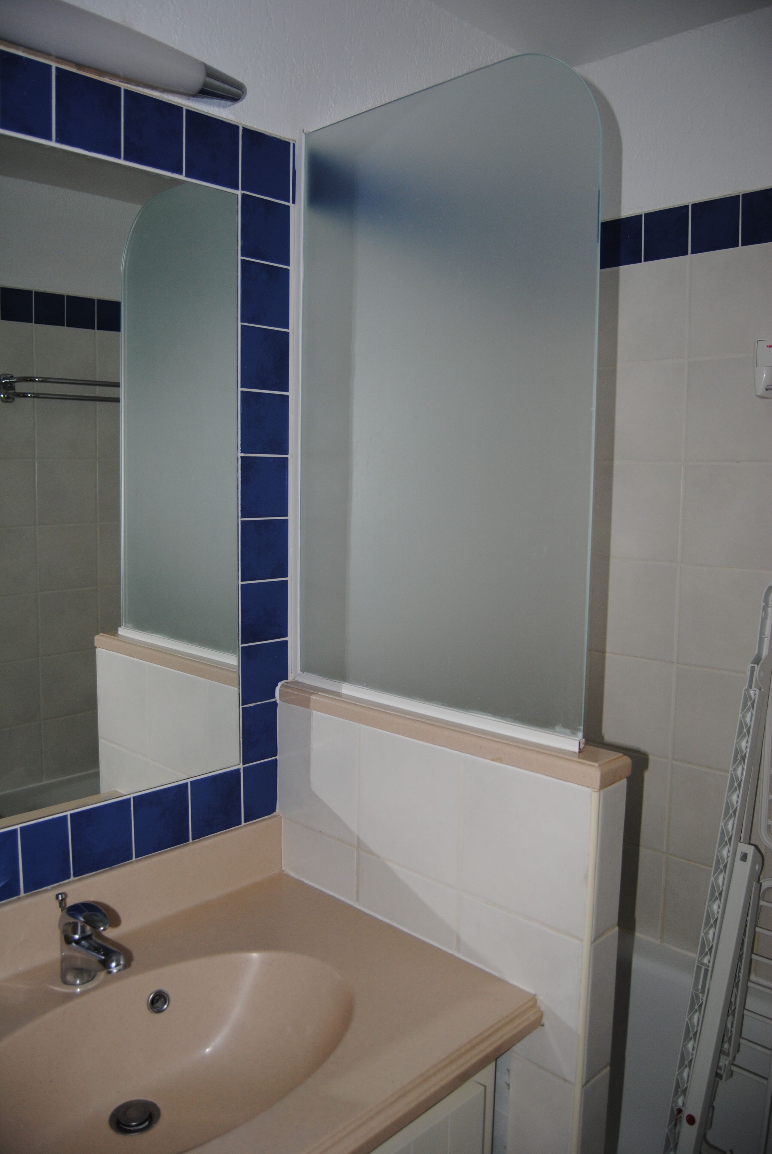 A bathroom with a beige sink, a mirror, and blue-tiled walls.