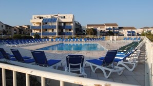 A swimming pool area with blue and white lounge chairs arranged around it, surrounded by multi-story buildings with balconies. - Apartment by the sea, Bleu Marine Lacanau Ocean residence France (Lacanau Océan)