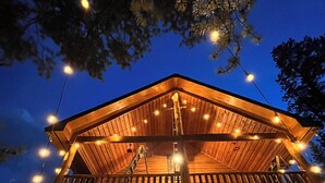 Une cabane en bois dotée d’un balcon, de guirlandes lumineuses et d’un escalier en bois.