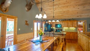 Une cuisine rustique avec des meubles en bois, un îlot central doté de tabourets, un luminaire suspendu et des têtes de cerf fixées au mur.