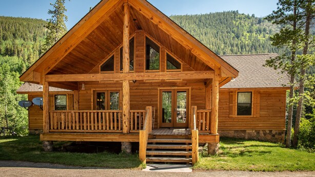 Une cabane en bois dotée d’un porche, de fondations en pierre et surplombant un paysage montagneux.