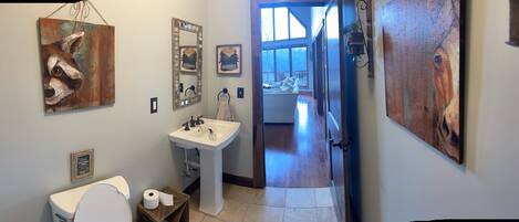 A bathroom with a toilet, sink, and mirror, with artwork on the walls and a view to a balcony.