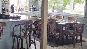 A kitchen with a dining area, featuring a large window, wooden chairs, and a coffee station. - GULF FRONT PENSACOLA BEACH 4BD/3BA HEATED POOL PET FRIENDLY (Gulf Breeze)