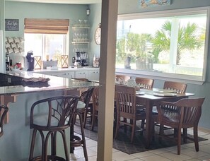 A kitchen with a dining area, featuring a large window, wooden chairs, and a coffee station.