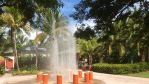 A water fountain surrounded by orange bollards in a park with palm trees and a building in the background. - Paradise Found, Unique Location (Key Biscayne)