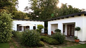 A modern house with a garden, featuring a stone pathway, potted plants, and a large umbrella. - Plumbago Guest House (Mbombela)